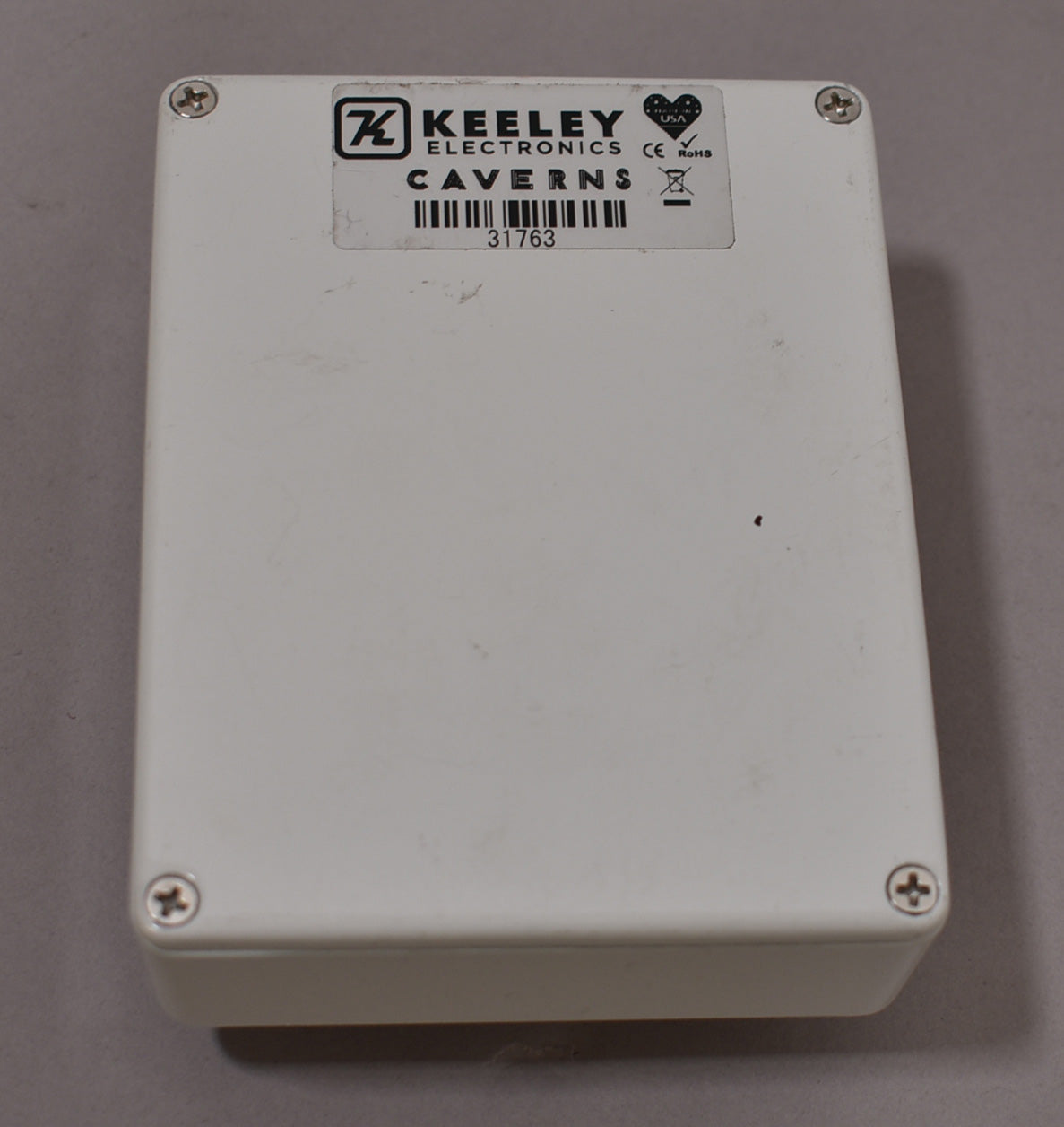 The white pedal's back is visible, secured by four silver Phillips head screws, with a black and white label.