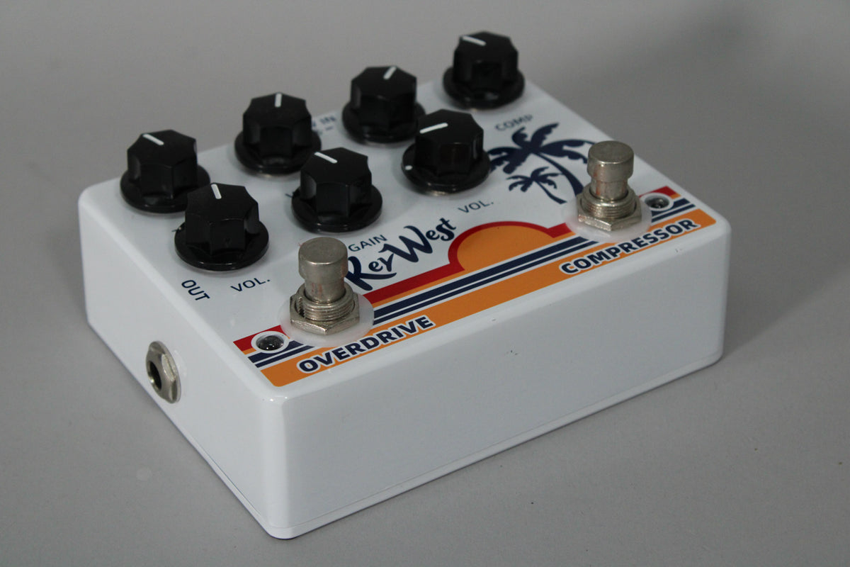 A white guitar pedal with a sunset and palm tree graphic, 8 black knobs, and two silver footswitches, viewed from the front right.