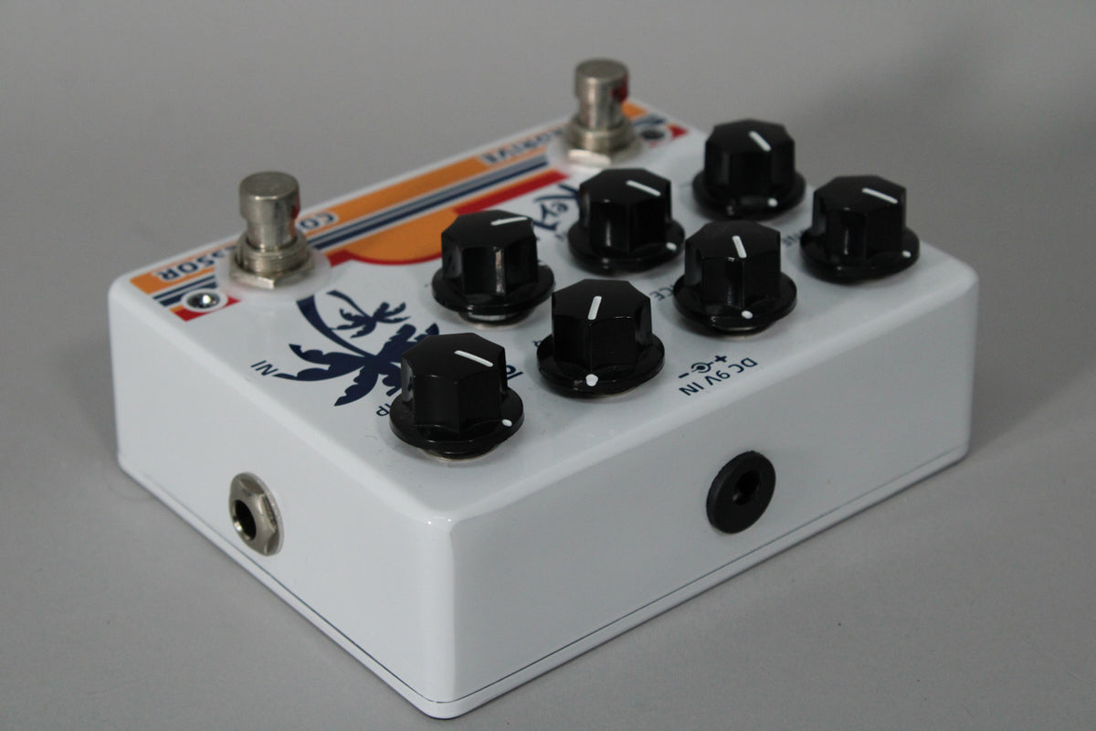 A white pedal with a blue palm tree graphic, two footswitches, and six black control knobs, viewed from the right.