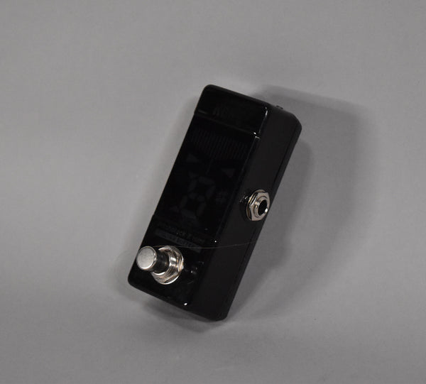 A glossy black mini tuner pedal, angled to show the top display, a chrome footswitch, and a side input jack.