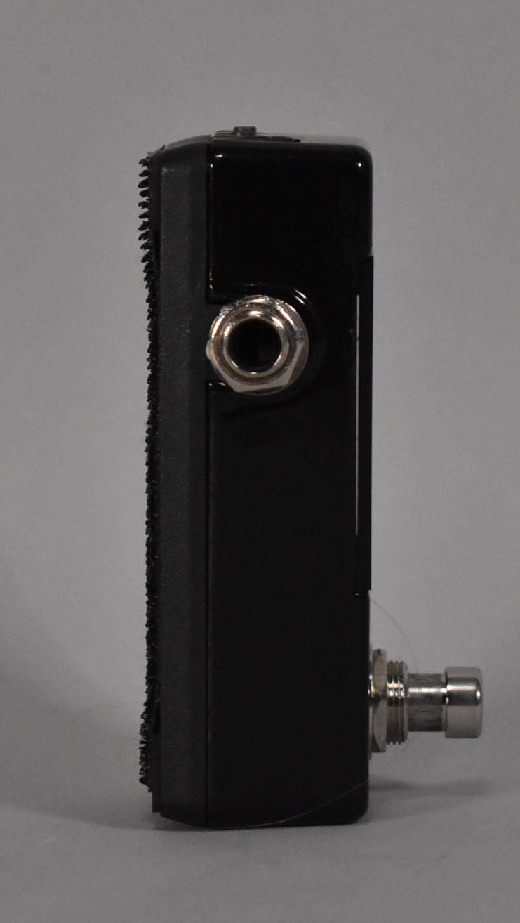 Side view of a black Korg Pitch Black X Mini Tuner Pedal with a silver input jack and a silver footswitch.