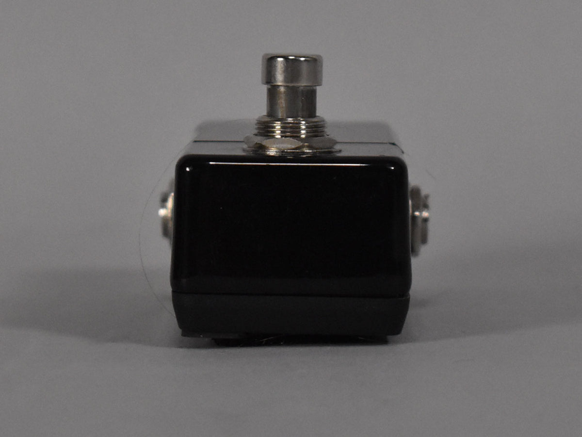 The mini tuner pedal is shown from the front, featuring a glossy black top and matte black base, with a silver footswitch.