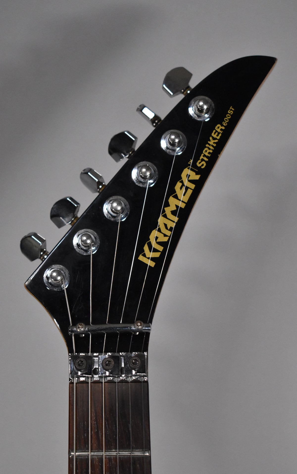 The black gloss headstock with gold lettering and six chrome tuners shows light wear, with a locking nut at the base.