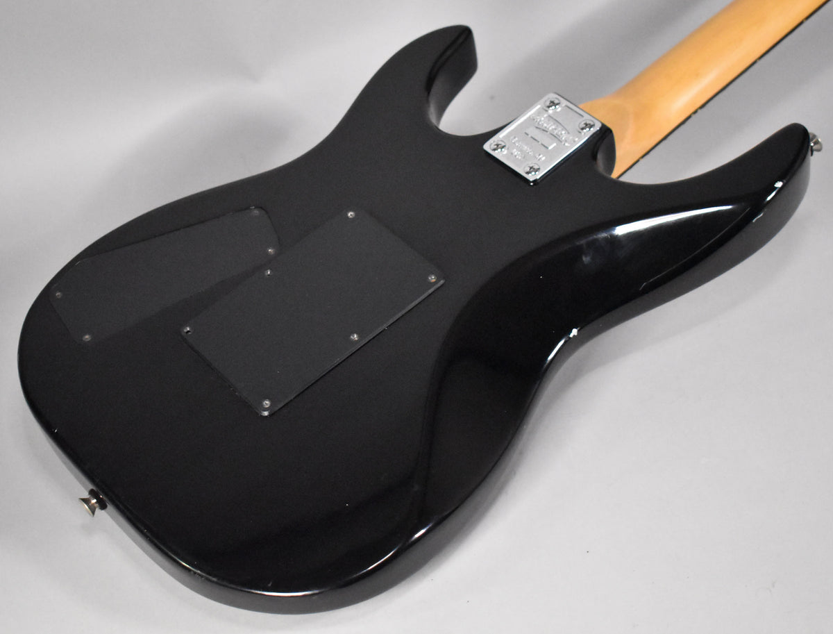 The guitar's black body, with a matte finish on the back, features two control cavity covers and a chrome neck plate with a visible scratch.