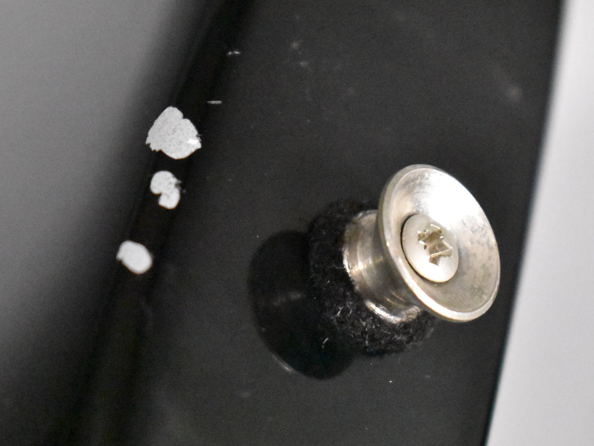 Close-up of the black guitar body showing a silver strap button with a felt washer and three small chips in the finish nearby.