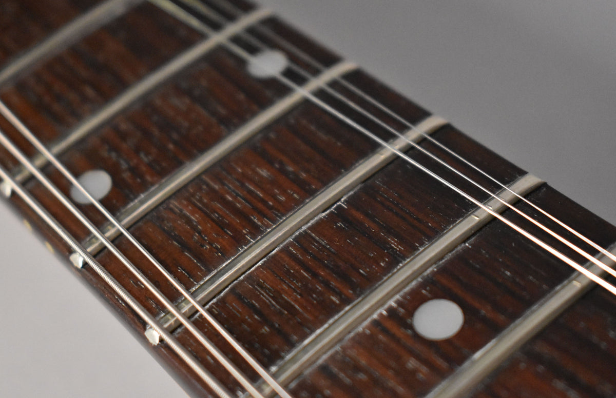 Close-up of the dark brown fretboard with white dot inlays and silver frets, showing wear and light scratches on the wood.