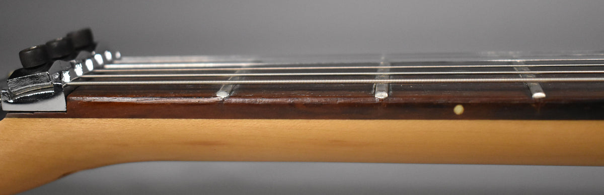Close-up of the guitar's neck and fretboard from the side, showing the locking nut, strings, dark fretboard, and light wood neck.