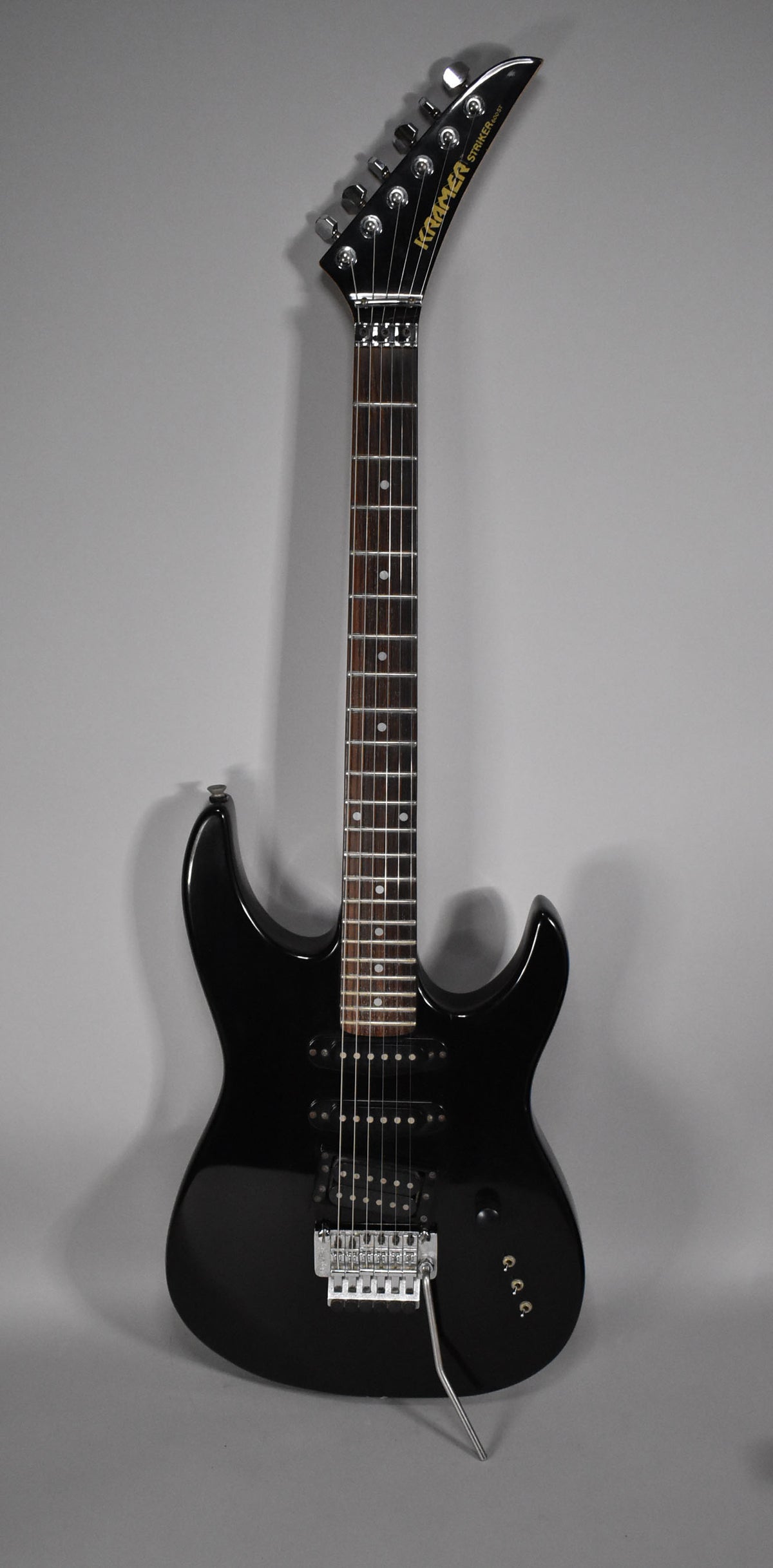 Full view of a black electric guitar with a glossy finish, featuring a pointed headstock, two humbuckers, and a tremolo bridge.