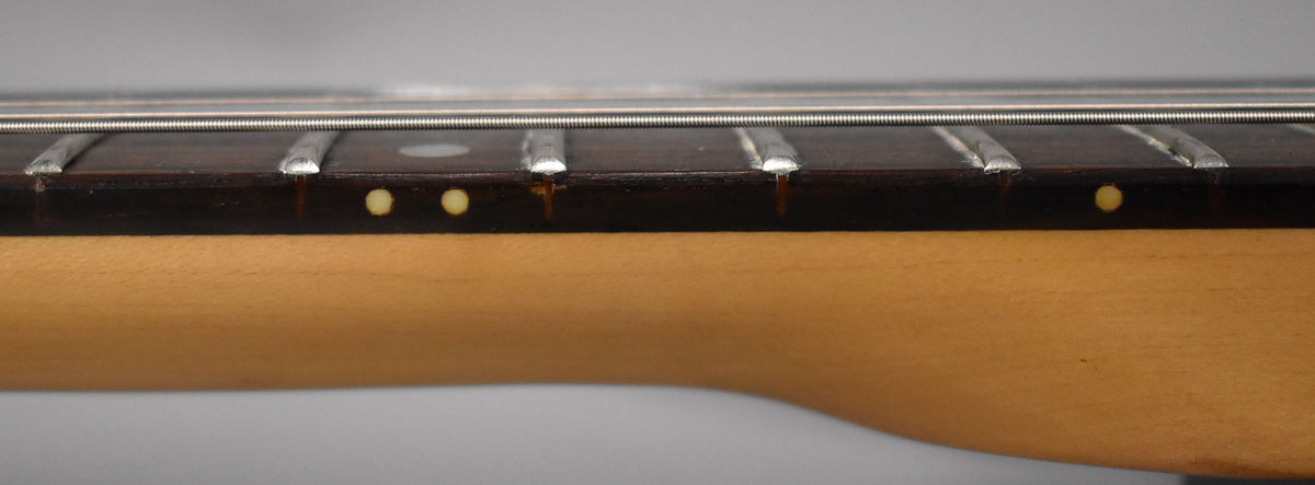 Close-up of the dark fretboard and light maple neck, showing three small yellow dot inlays and some wear near the frets.