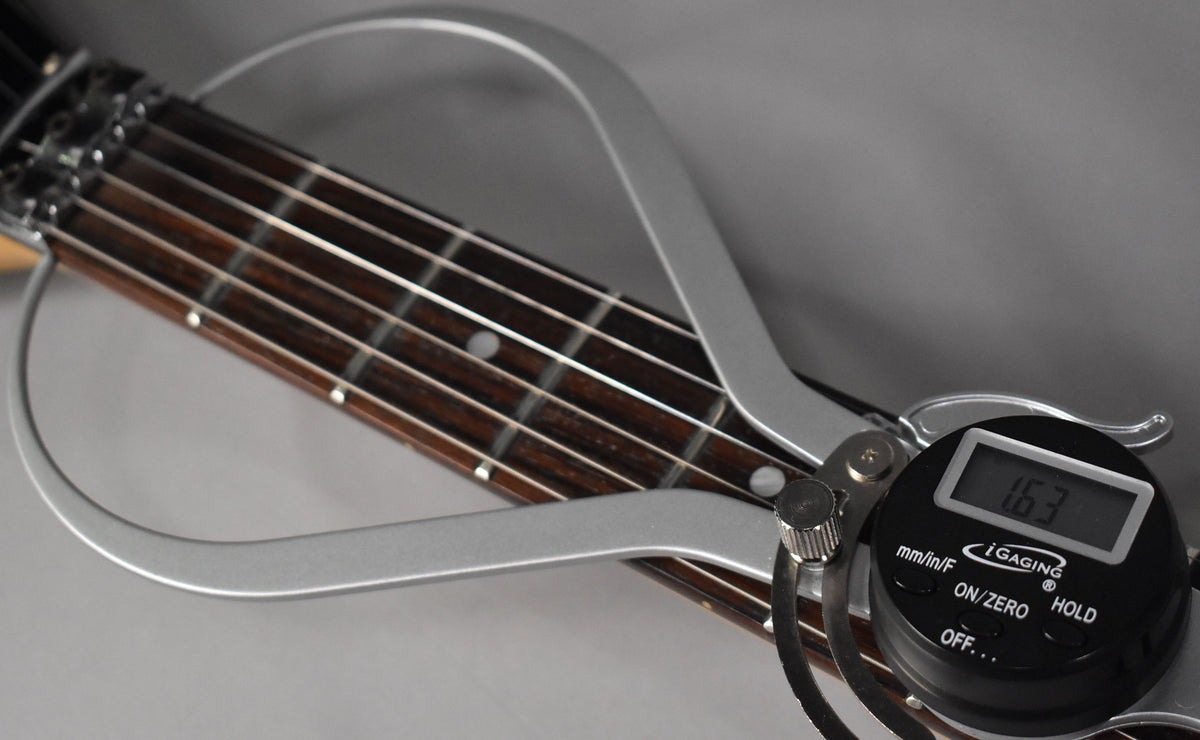 Close-up of the guitar's dark fretboard with white dot inlays, measured by a silver radius gauge showing "16.3" on its digital display.