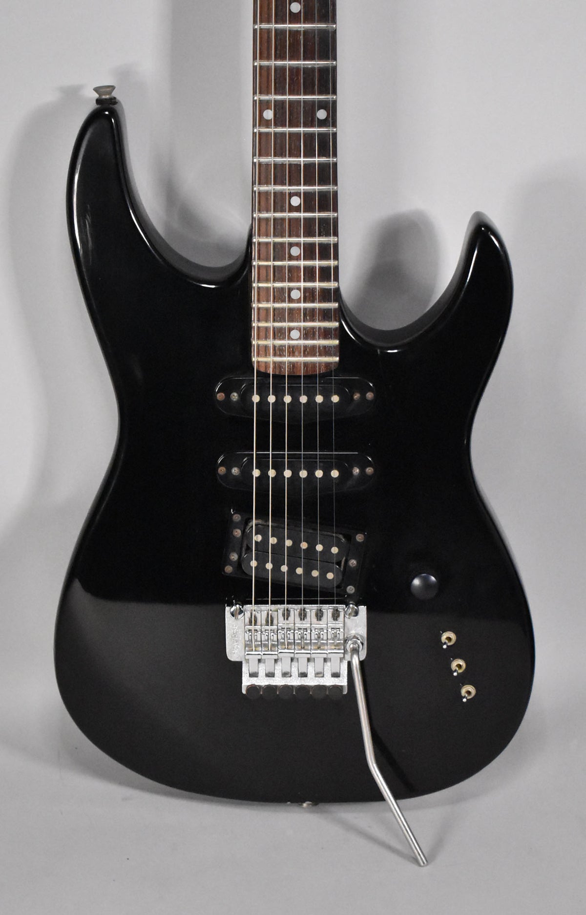 A black electric guitar with a rosewood fretboard, three pickups, a chrome tremolo bridge, and three gold control knobs.