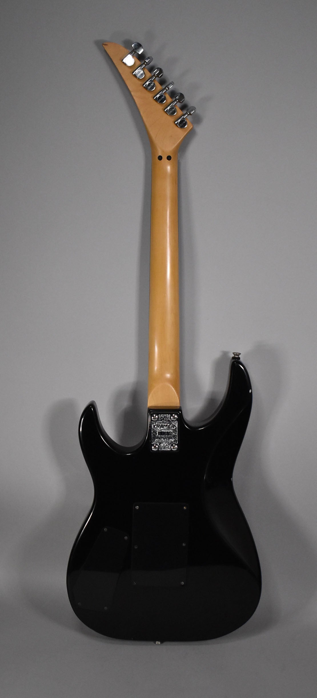 Full rear view of a black electric guitar with a glossy finish, showing the natural wood neck and headstock with six chrome tuners.