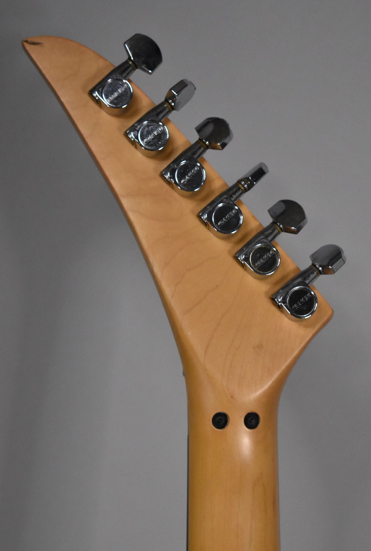 The back of a light wood headstock with six chrome tuners, angled left, showing a small chip on the top left edge.