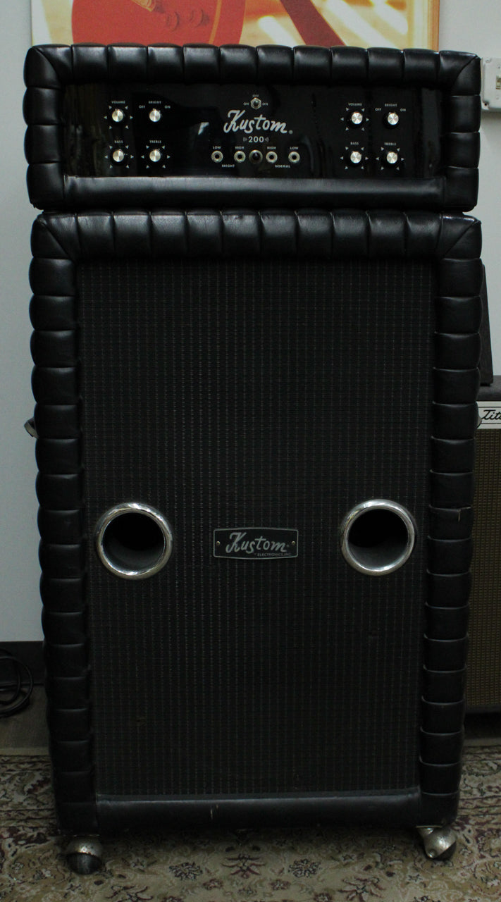 Full front view of a black tuck-and-roll amp head and matching 2x15 cab with two chrome ports and casters.