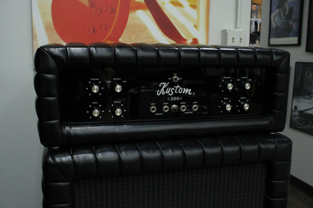 The black tuck-and-roll amp head sits atop its matching cab, showing its shiny black control panel with silver knobs and input jacks.