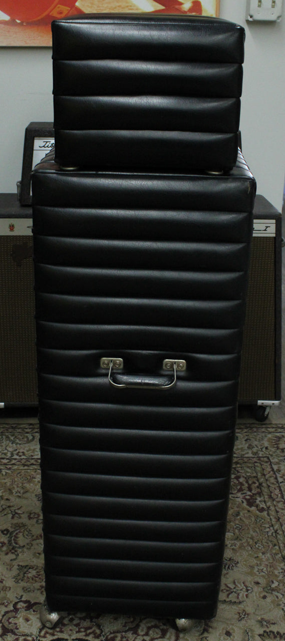 Full front view of the black tuck-and-roll head stacked on the matching 2x15 cab, showing the cab's metal handle and casters.