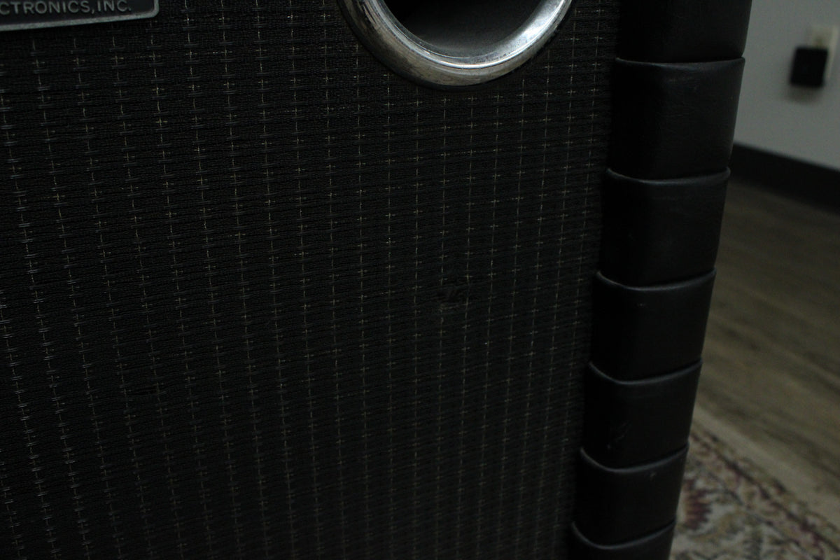 Close-up of the black grill cloth with a subtle grid pattern, a silver port, and the black tuck-and-roll corner trim.