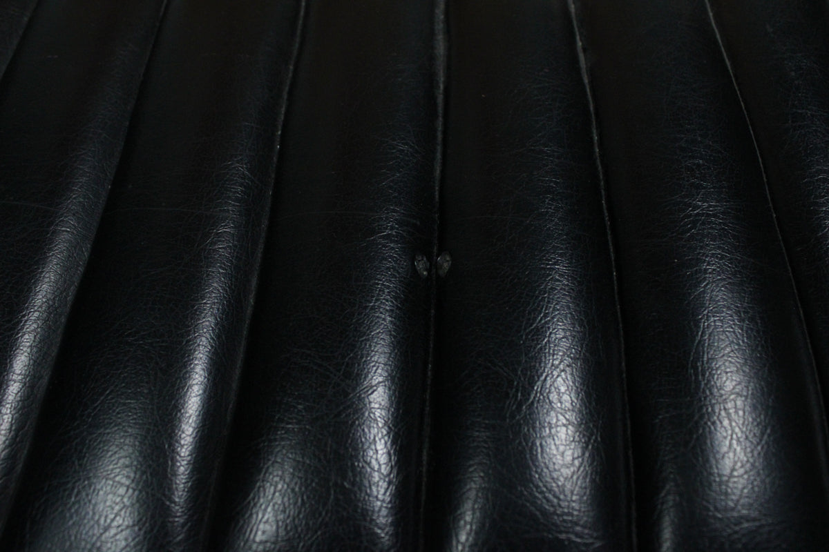 Close-up of the black tuck-and-roll vinyl, showing a small tear in the center of one of the vertical pleats.