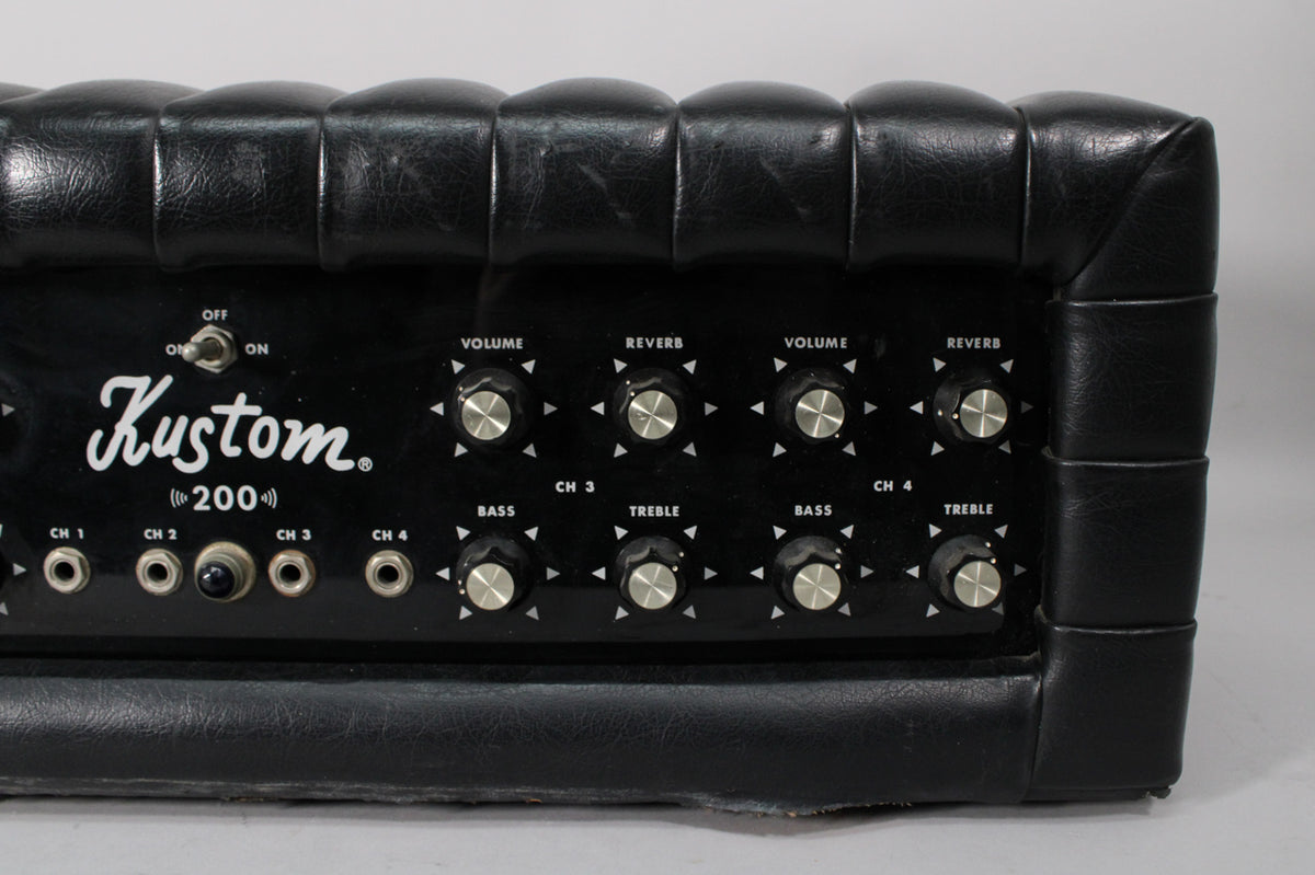 Close-up of the black amp's front panel, showing the power switch, four input jacks, and eight silver-capped control knobs.