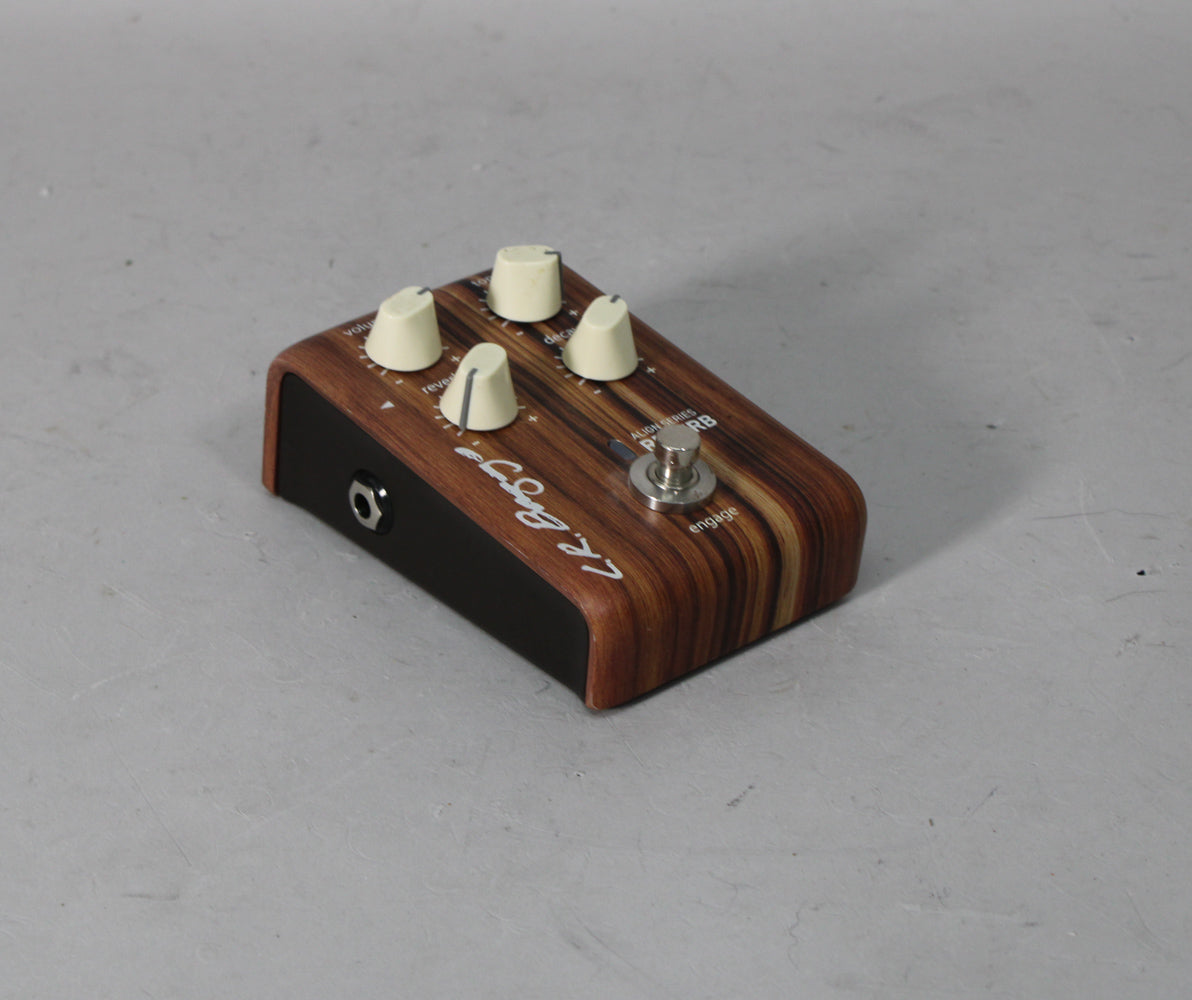 A compact pedal with a dark woodgrain top, black sides, four cream knobs, and a silver footswitch, viewed from above and slightly to the left.