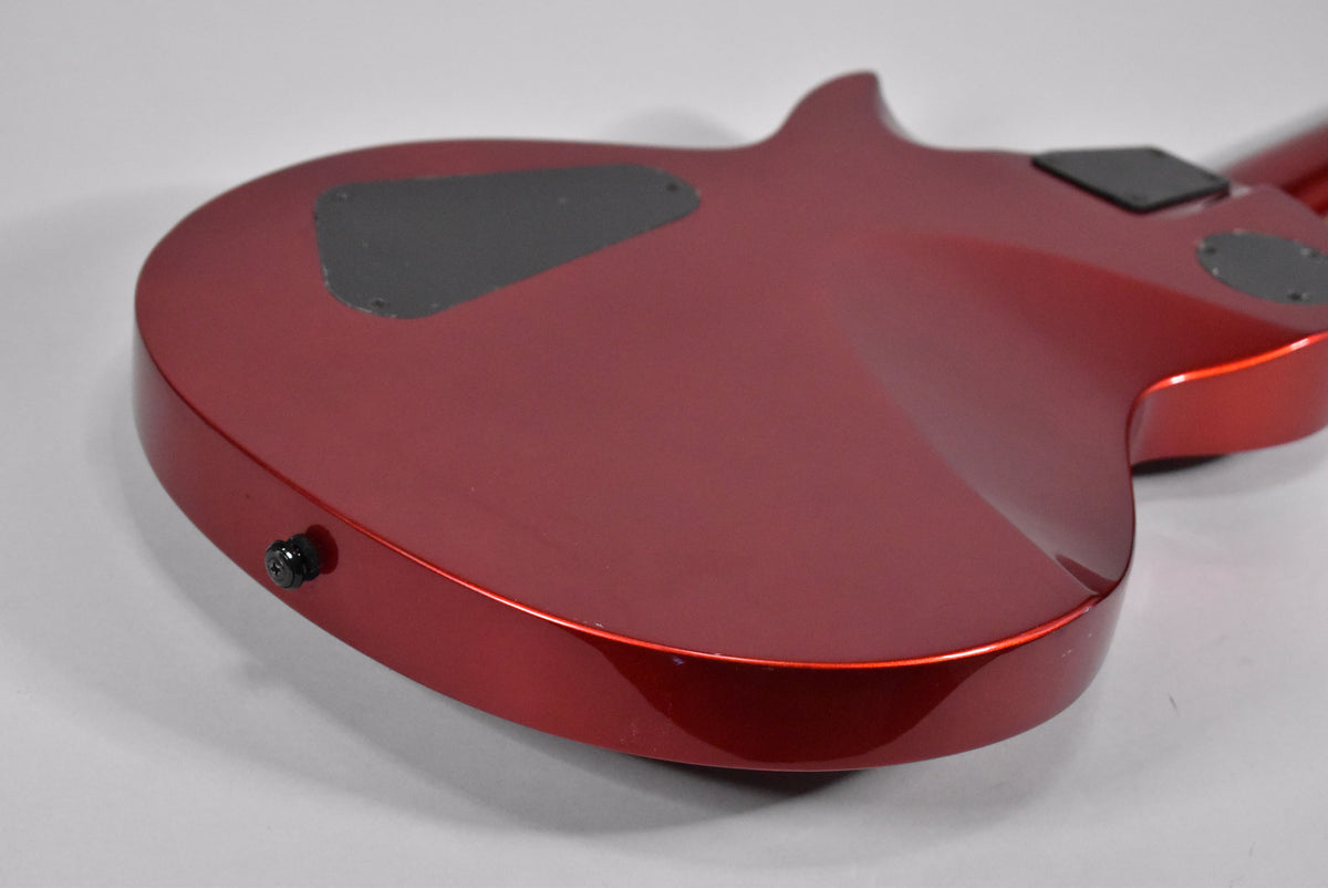 The back of the red metallic guitar body, angled from the lower left, shows a black output jack and two black control cavity covers.