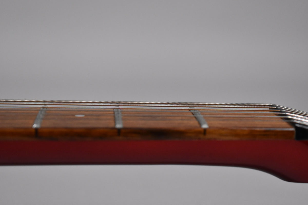 Close-up of the guitar's dark wood fretboard and silver frets, viewed from the side, with a glossy red finish visible below.