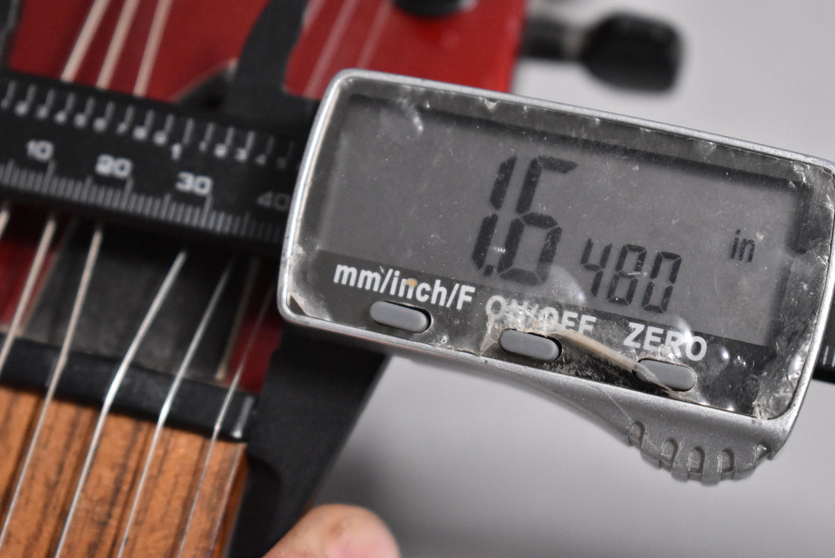 Close-up of a digital caliper measuring the string height on the guitar's fretboard, showing "1.6" and "480 in" on its screen.