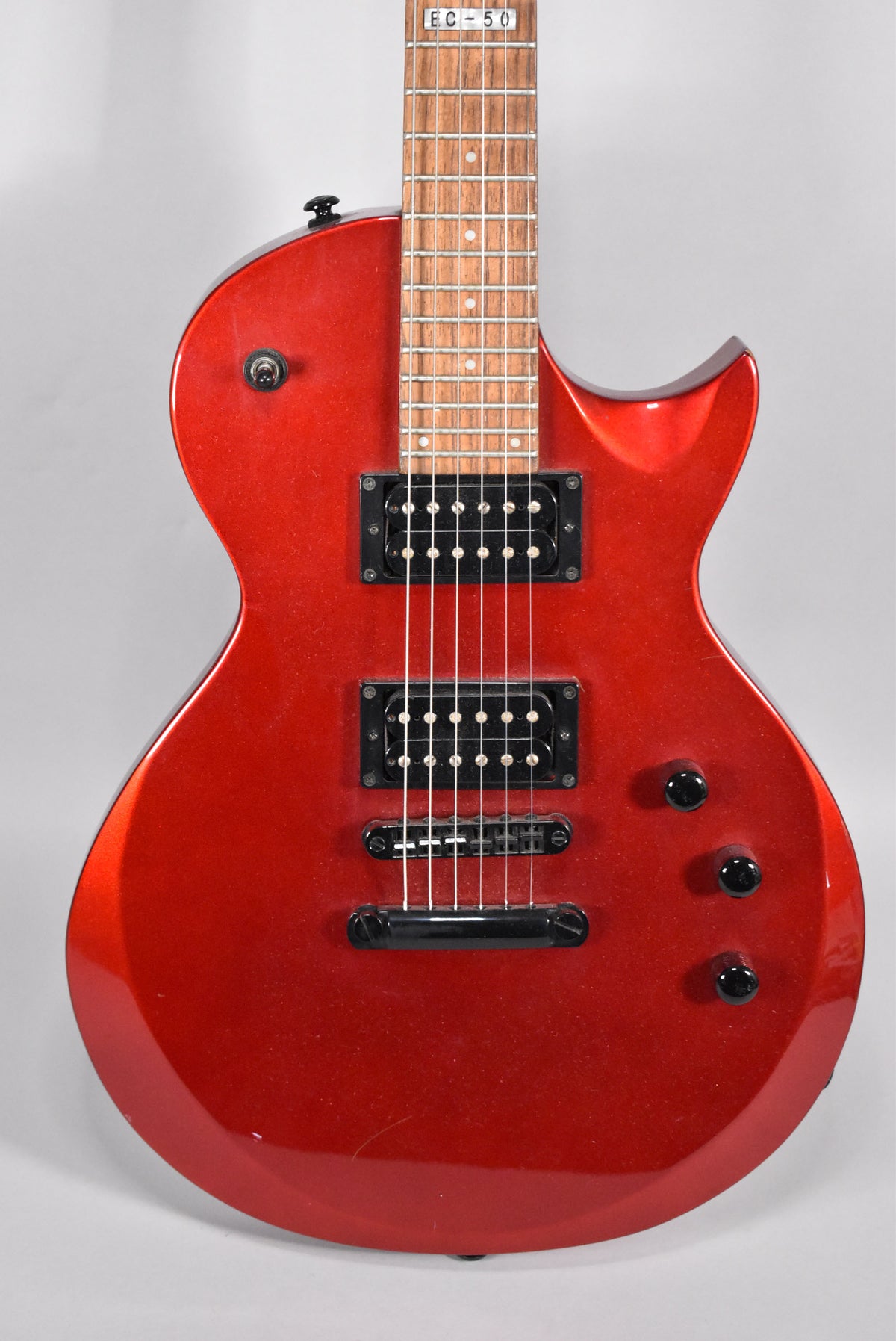 The red metallic-finish electric guitar is shown from the front, with two black humbucker pickups and three black control knobs.