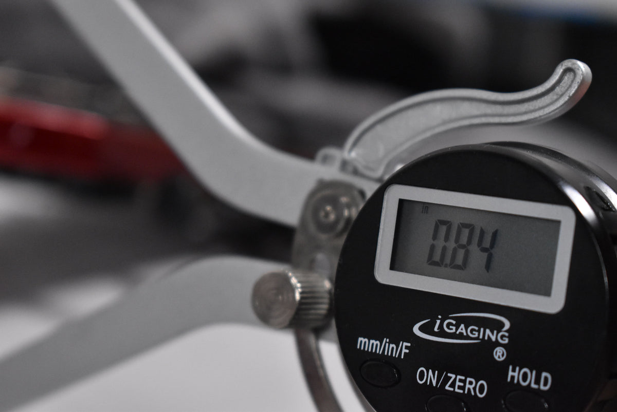 A digital caliper measures 0.84 inches, with a blurred red guitar body visible in the background.