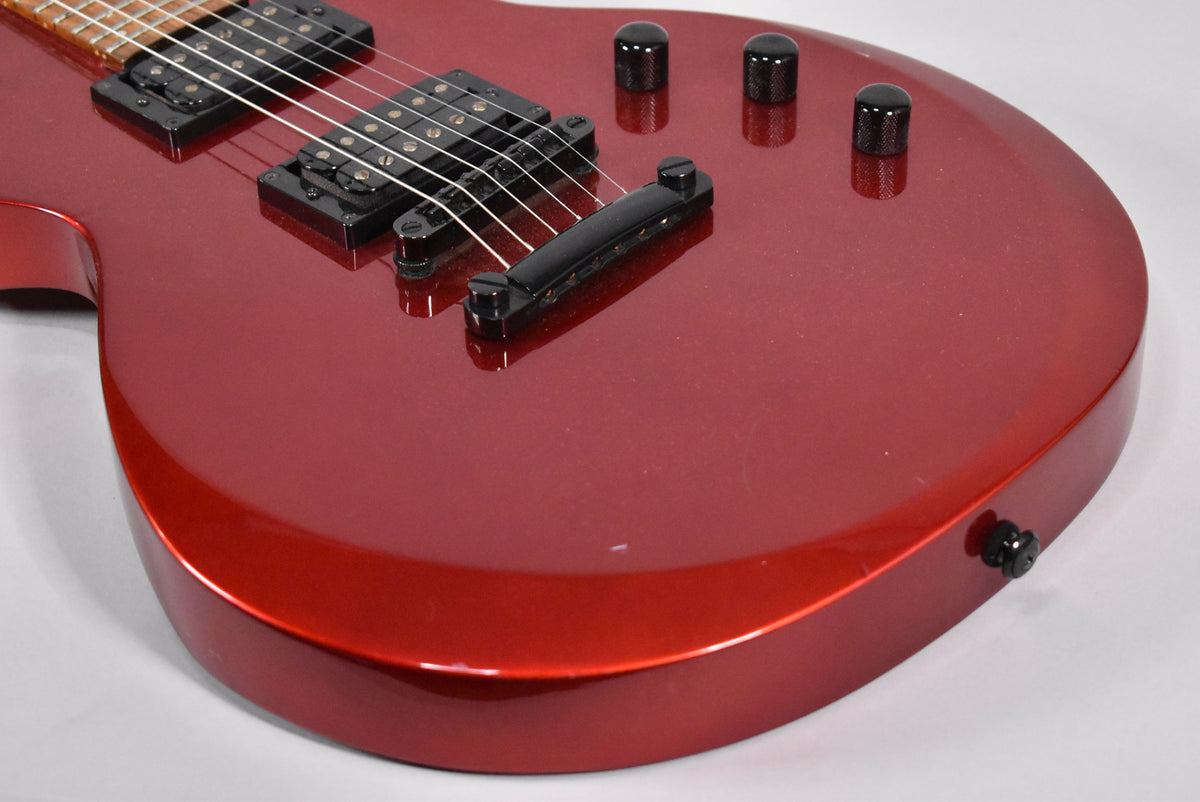 Close-up of the metallic red guitar body, showing black humbucker pickups, tune-o-matic bridge, four knurled control knobs, and light surface wear.