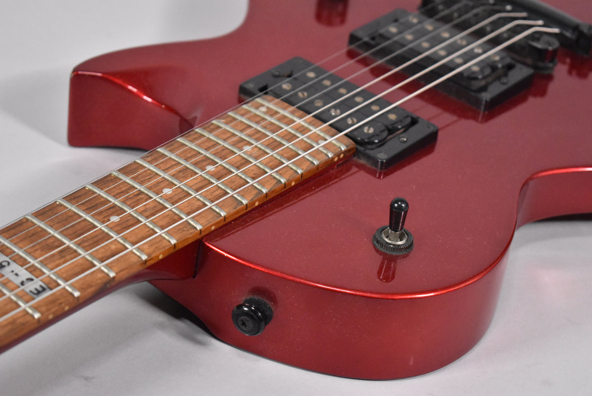 Close-up of the metallic red body and fretboard, showing two black humbucker pickups and a three-way toggle switch.
