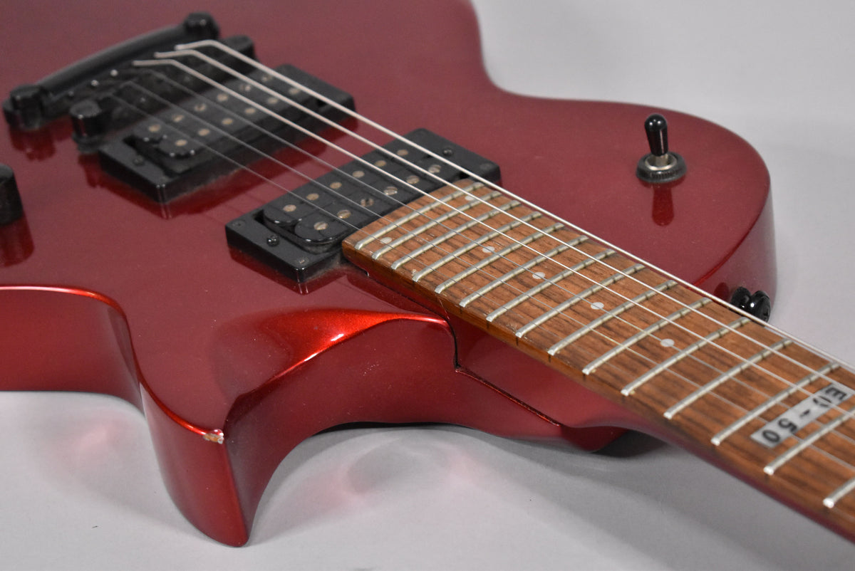 Close-up of the metallic red body and fretboard, showing two black humbucker pickups, a toggle switch, and a chip on the lower horn.