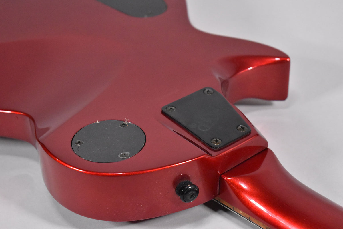 The guitar's metallic red back shows two black control plates, a black output jack, and light wear around the screws.