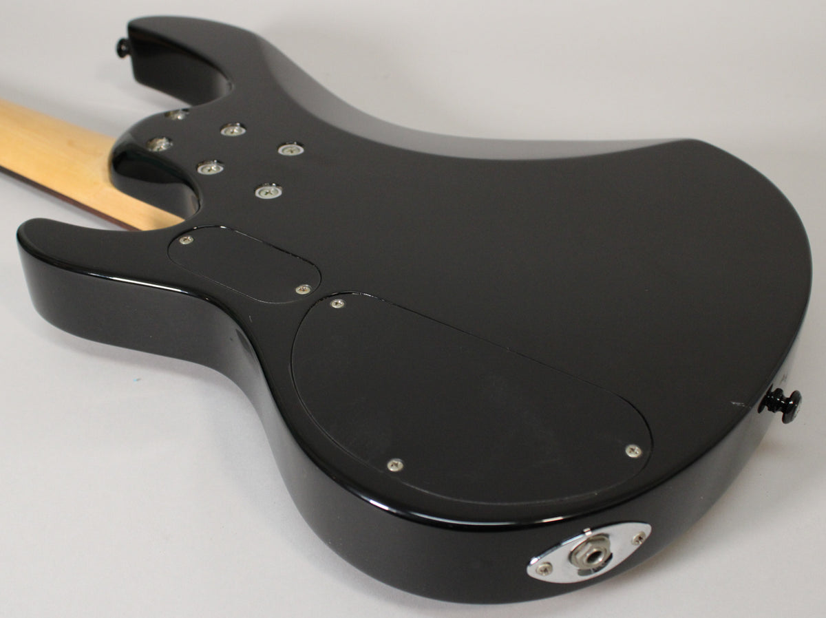 The black bass guitar's glossy back shows two control cavity covers, a chrome output jack, and a light scratch near the strap button.