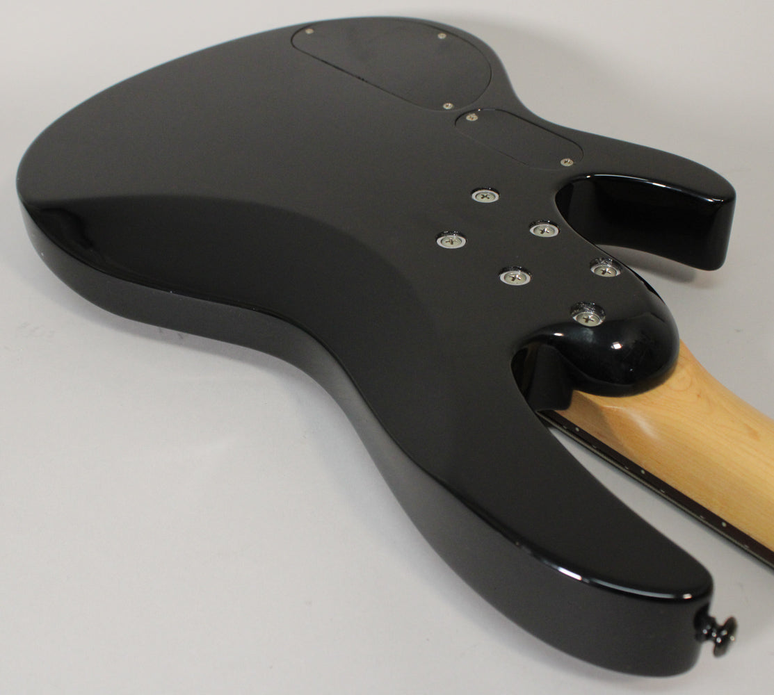 The glossy black bass guitar body is viewed from the back, angled to show the neck joint, control cavity, and strap button.