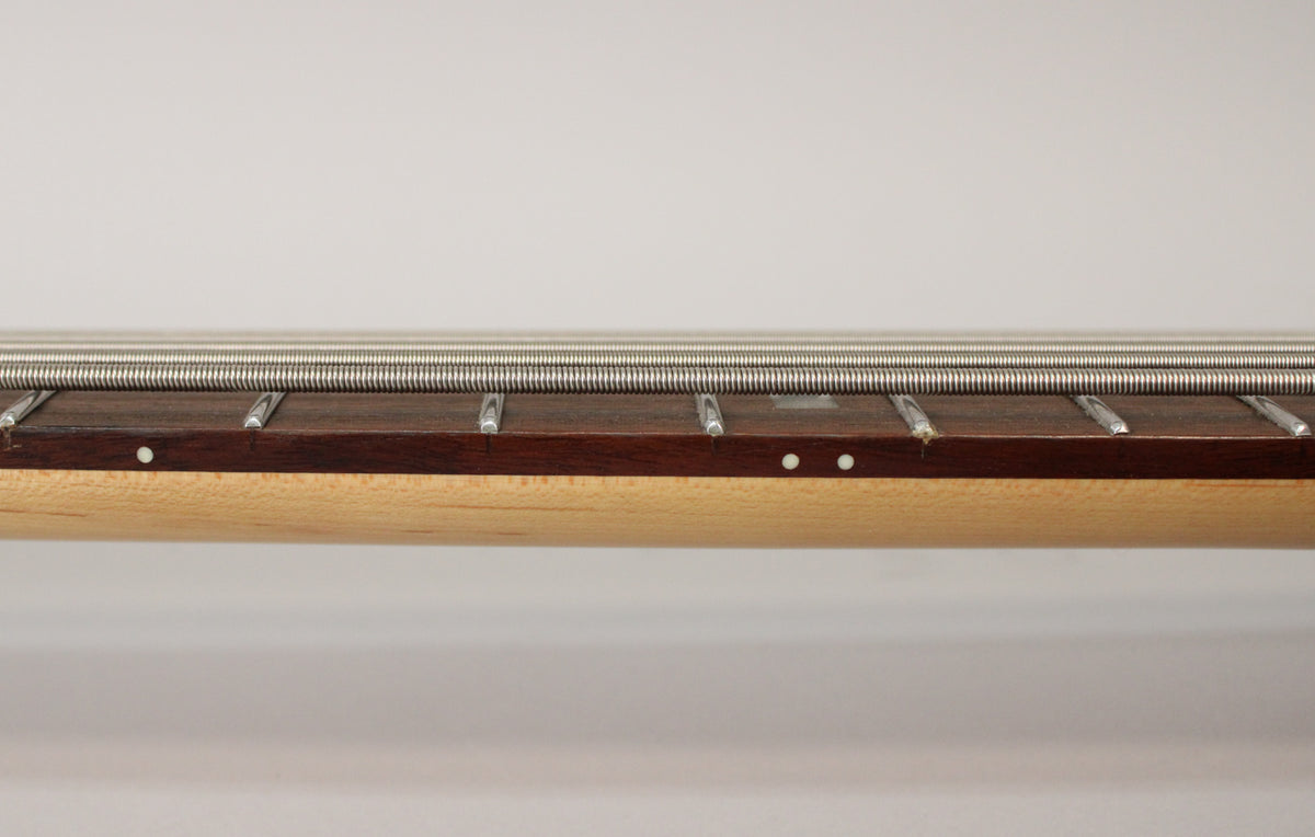 Close-up of the bass neck from the side, showing the light maple neck, dark rosewood fretboard, and four silver strings.
