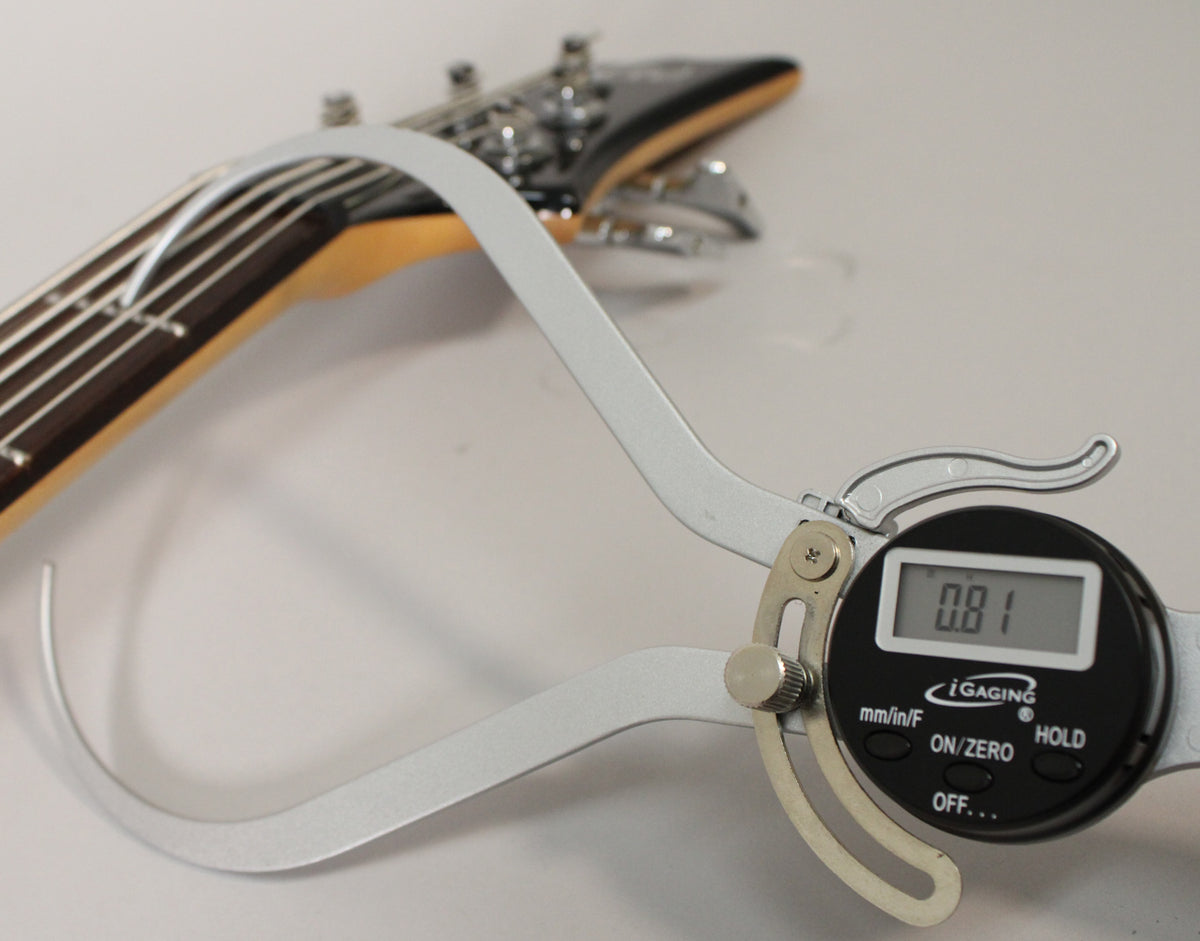 A digital caliper measures the bass neck's thickness at 0.81 inches, with the headstock and tuning pegs visible in the background.