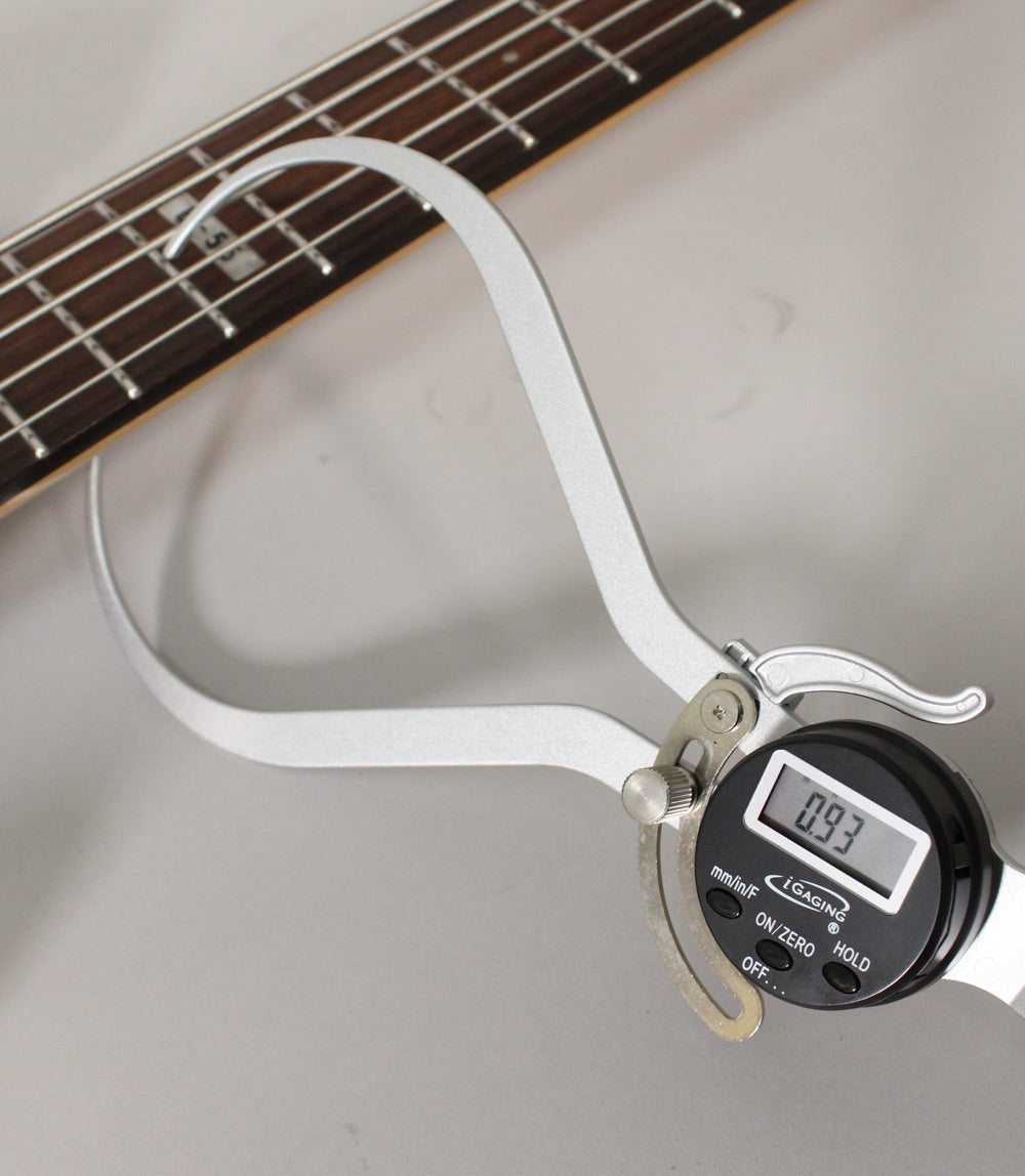 A digital caliper measures the bass's dark rosewood fretboard, showing 0.93 on its display.