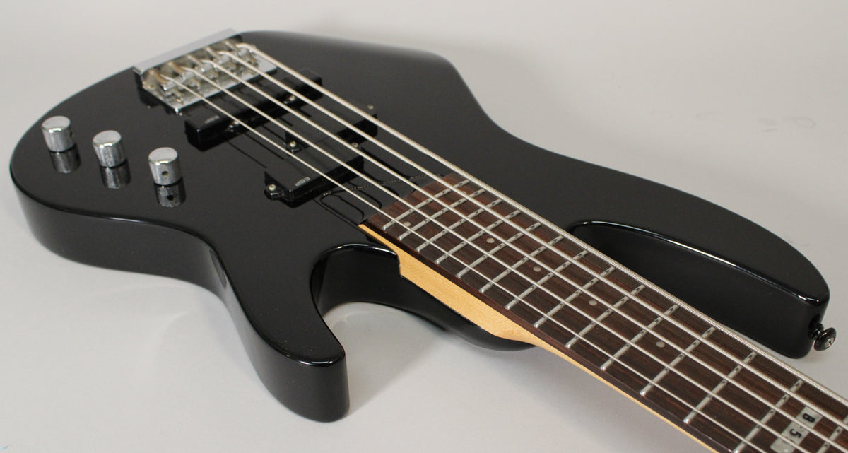 A black 5-string bass guitar, angled from the body to the neck, showing three chrome control knobs and two black pickups.