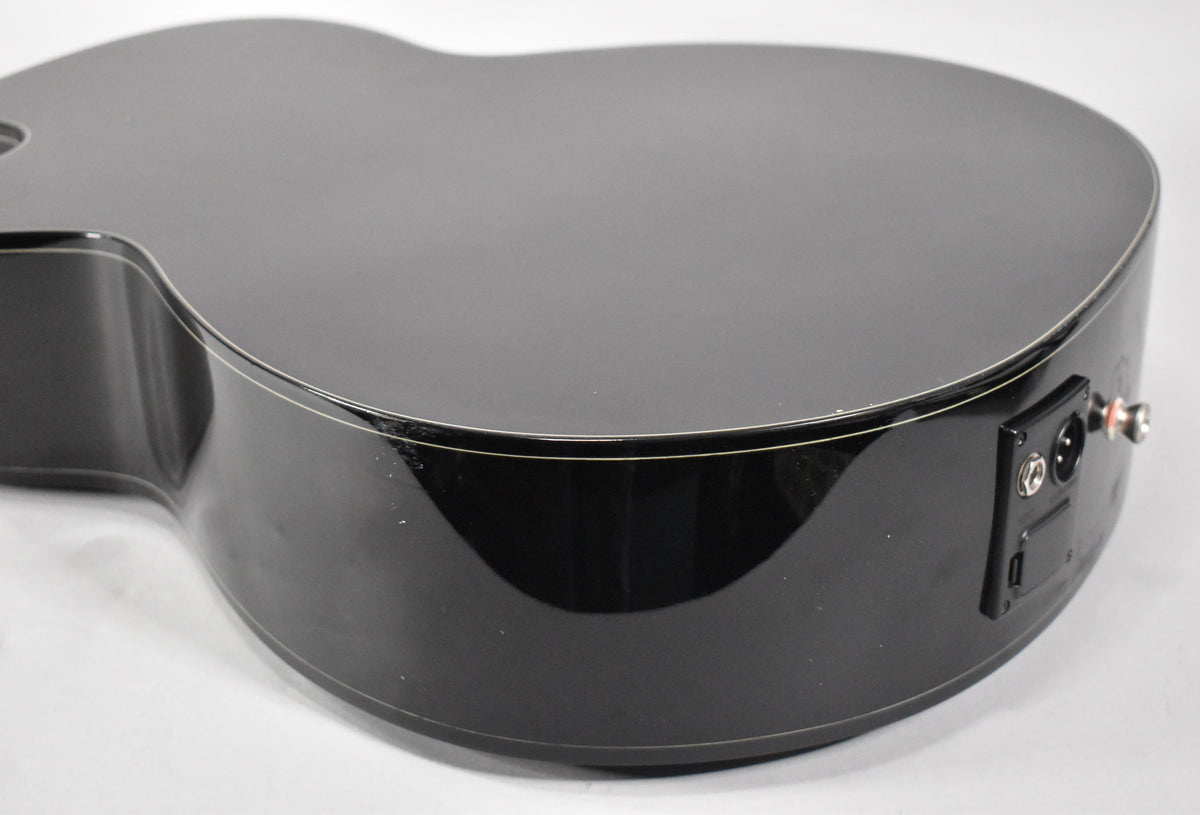 The black acoustic guitar's lower bout and side, showing the shiny finish, white binding, and a black output jack with XLR and 1/4" inputs.