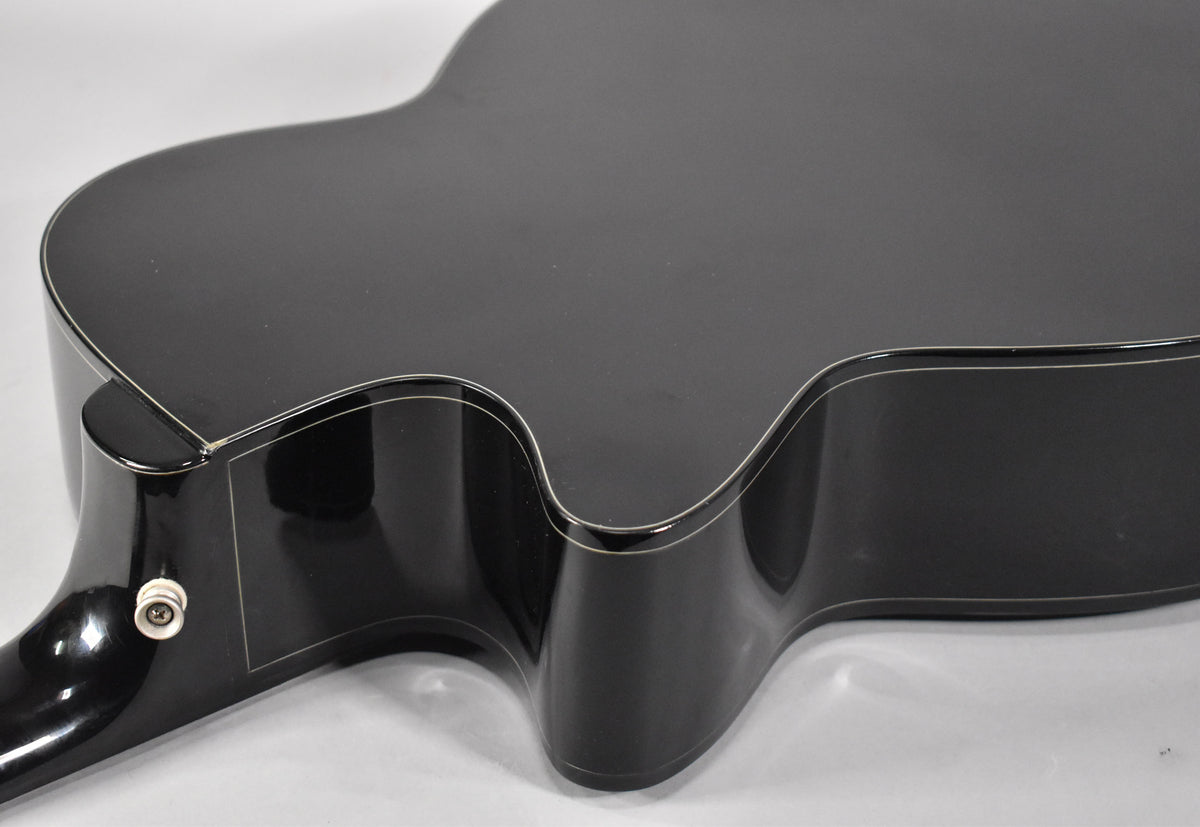 The black acoustic guitar's upper bout and cutaway are visible from above, showing white binding and a white endpin jack.