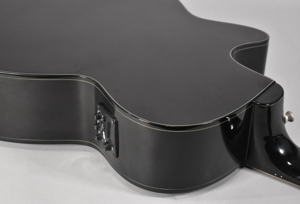 The black acoustic-electric guitar's lower bout and cutaway are shown from above, revealing the built-in preamp controls on the side.