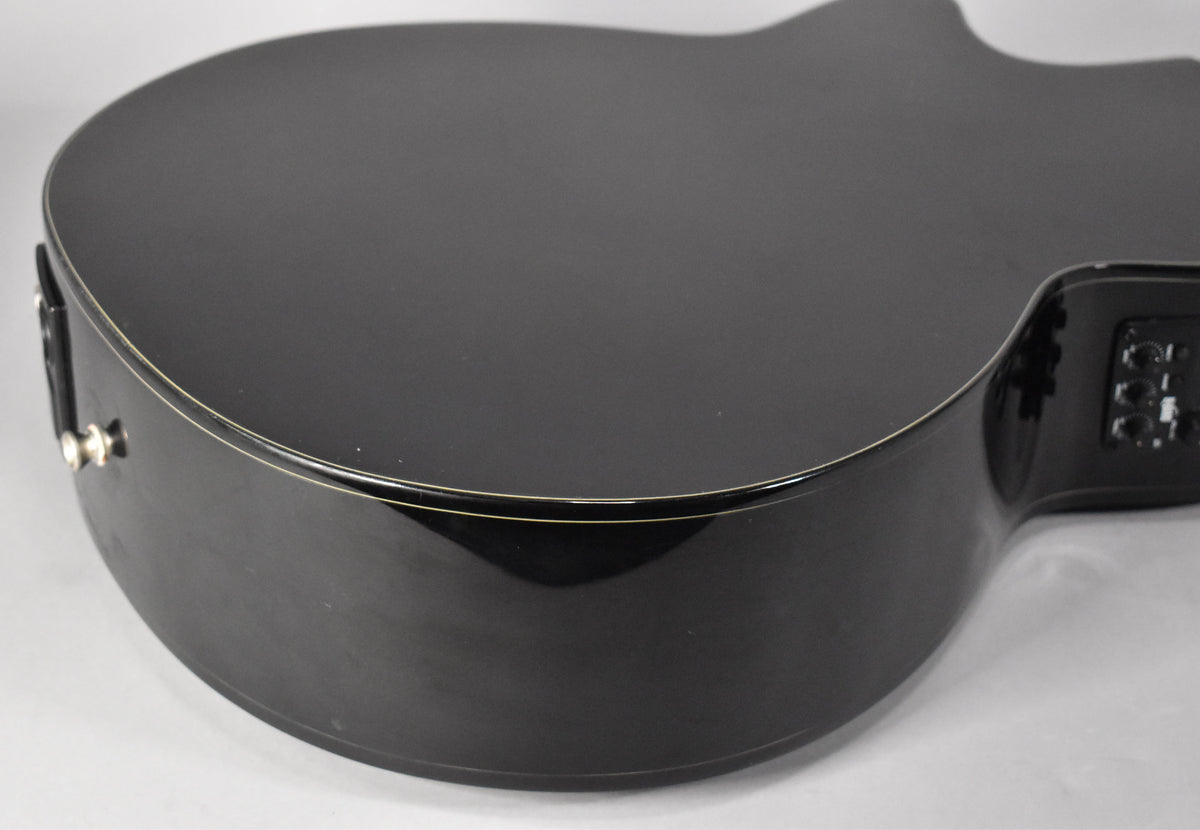 Close-up of the glossy black guitar body, showing the lower bout and cutaway with a preamp and output jack.