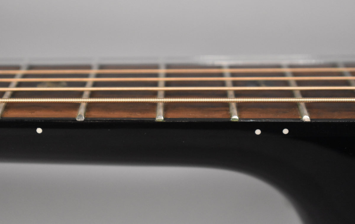 Close-up of the black guitar neck and dark fretboard, showing white side dot markers and light-colored strings.