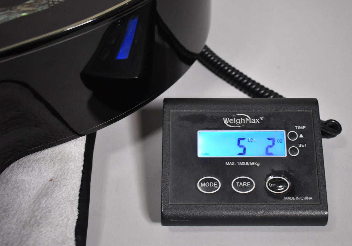 Close-up of the guitar's glossy black body, showing a blue illuminated preamp display and a digital scale reading 5 lbs 2 oz.
