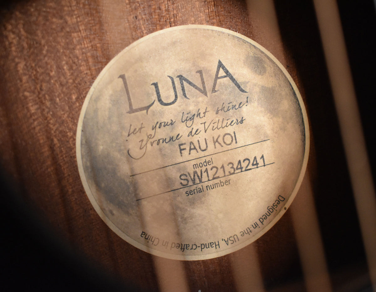 Close-up of the guitar's soundhole label, a circular sticker with a moon graphic and text, against the dark wood grain of the guitar's interior.