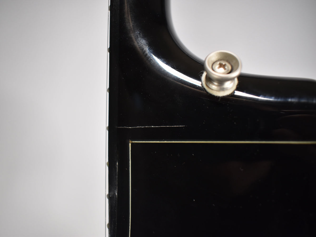 Close-up of the guitar's black gloss body and neck joint, showing a strap button and a fine crack in the finish.