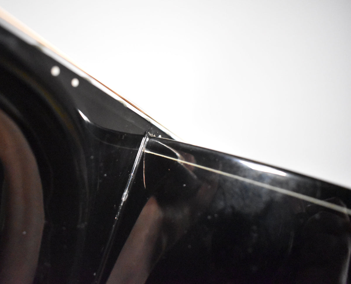Close-up of the black gloss finish on the guitar's neck heel, showing light scratches and a thin white binding line.