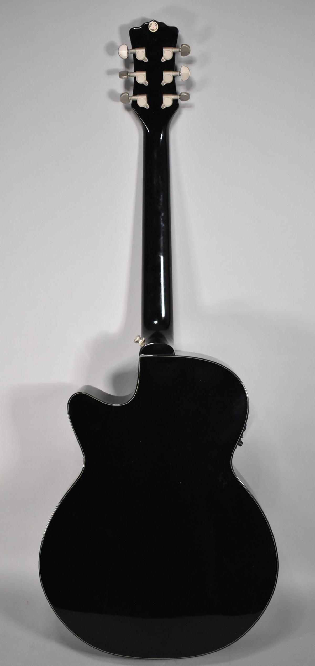 The back of a black acoustic-electric guitar with a cutaway, showing the headstock with six chrome tuners and a glossy finish.