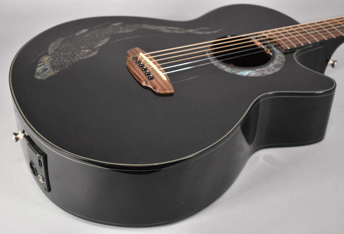 The black acoustic-electric guitar's body is angled, showing the koi graphic, abalone rosette, wooden bridge, and side-mounted preamp.